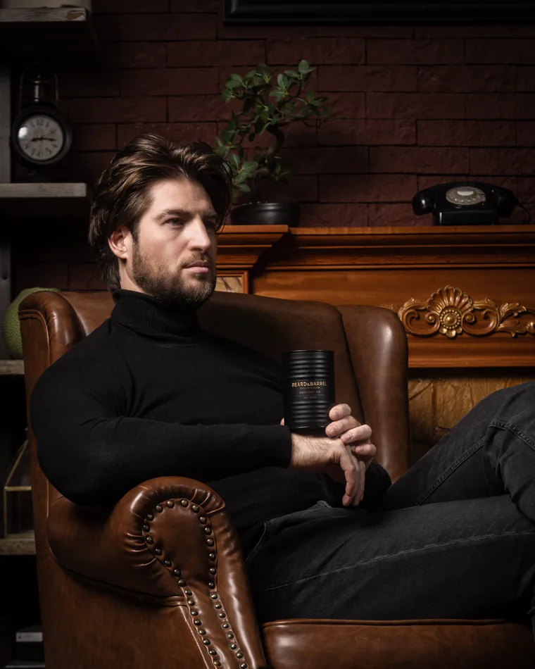 A man seated in a leather armchair holding the Beard & Barrel tin